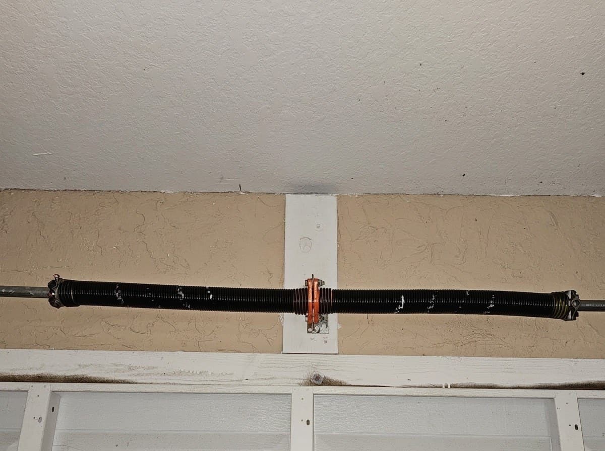 Torsion spring mounted above a closed white garage door, seen from inside