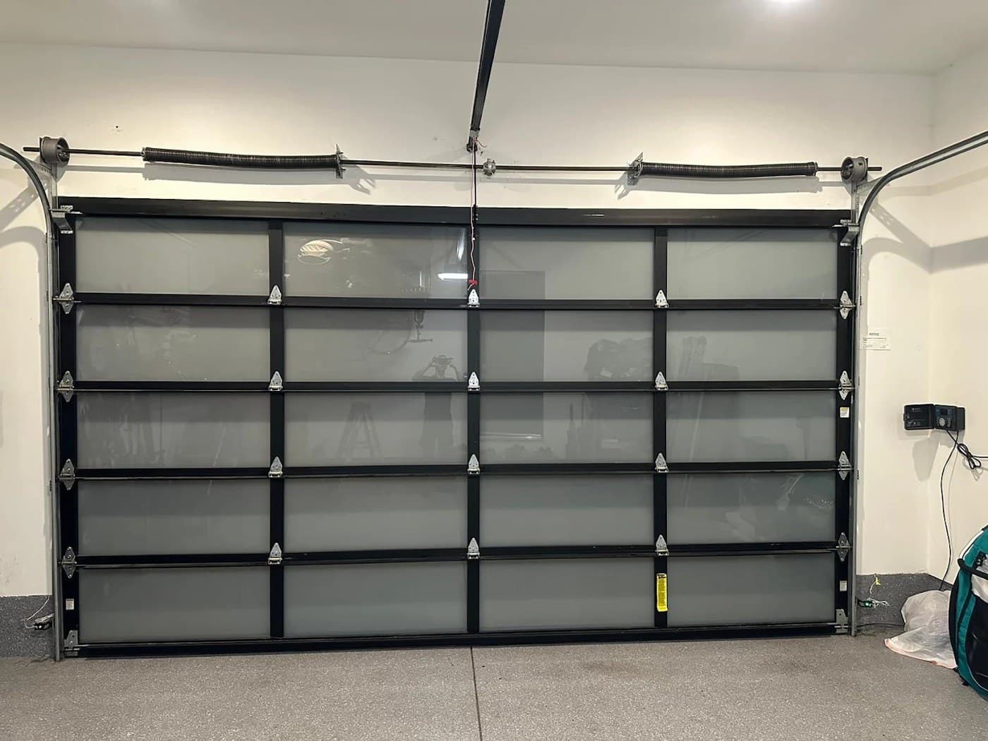 New garage door installation in Hollywood — full-view frosted glass and black aluminum door hung in the same opening, seen from inside