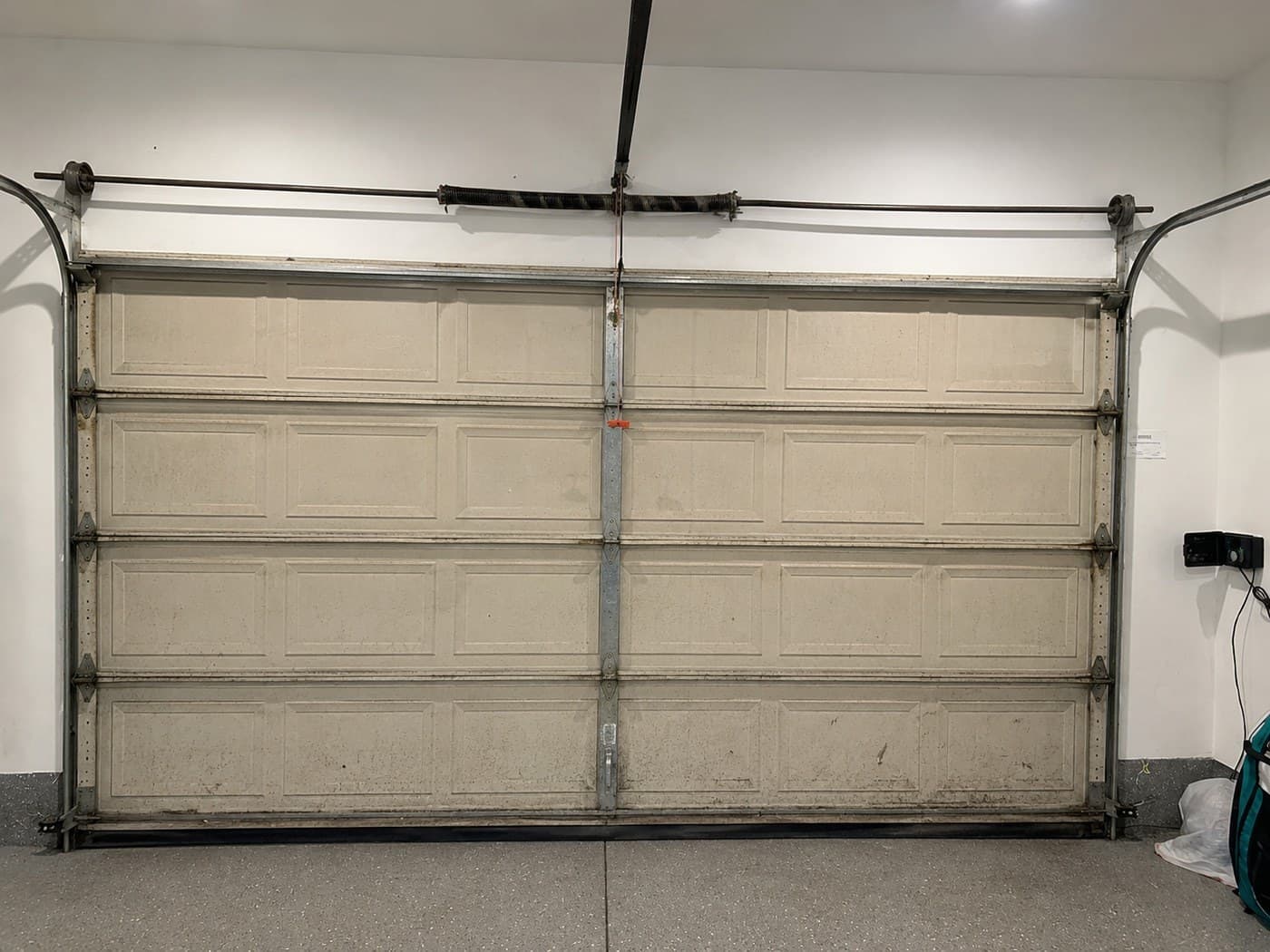 New garage door installation in Hollywood — old raised-panel steel door, stained and dented, seen from inside the garage before replacement